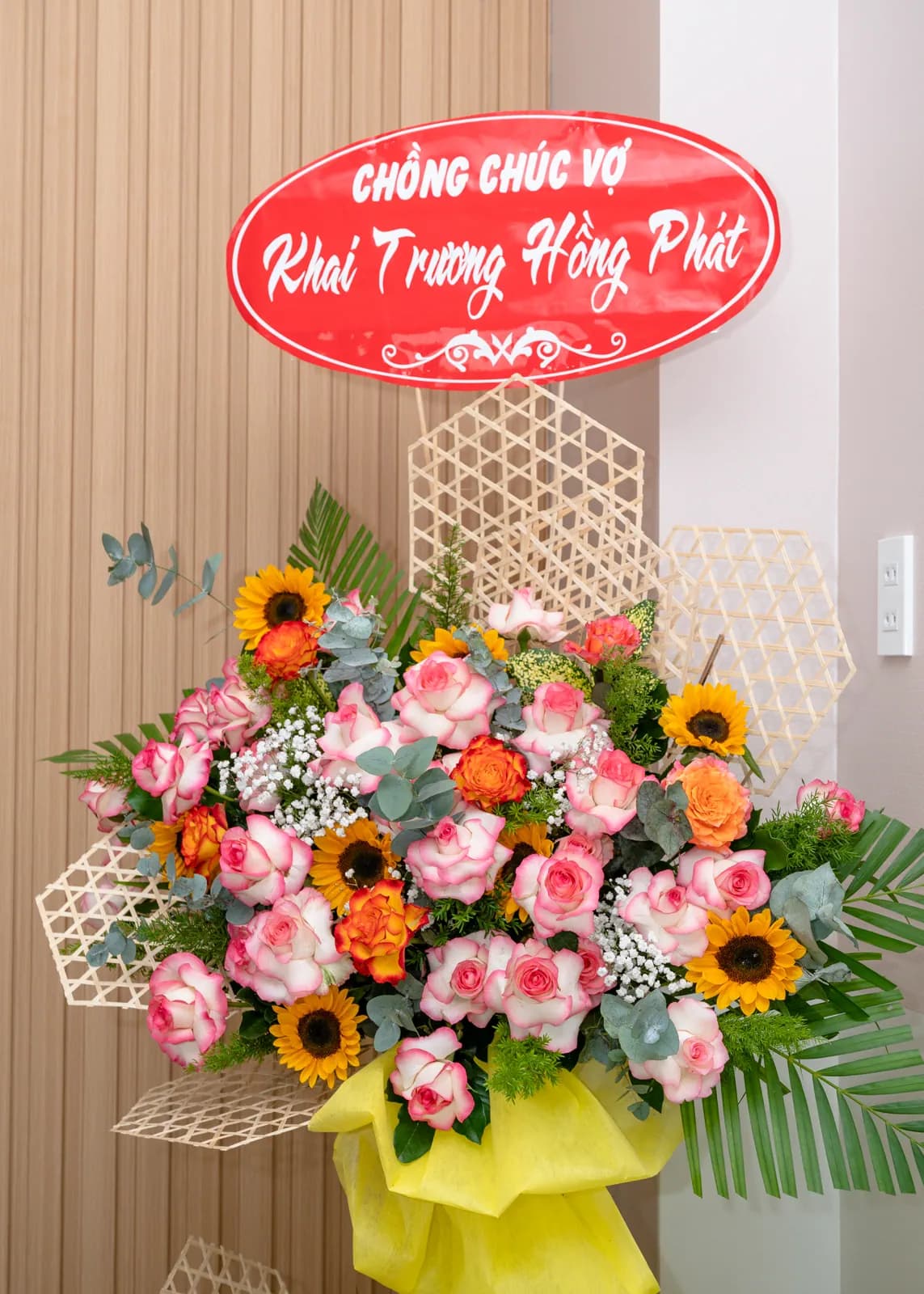 Lẵng hoa hướng dương, hoa hồng và lá xanh đặt cạnh vách gỗ