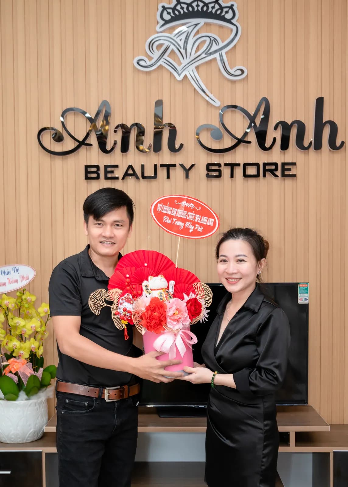 Hai người cầm bó hoa trước tường gỗ có bảng hiệu